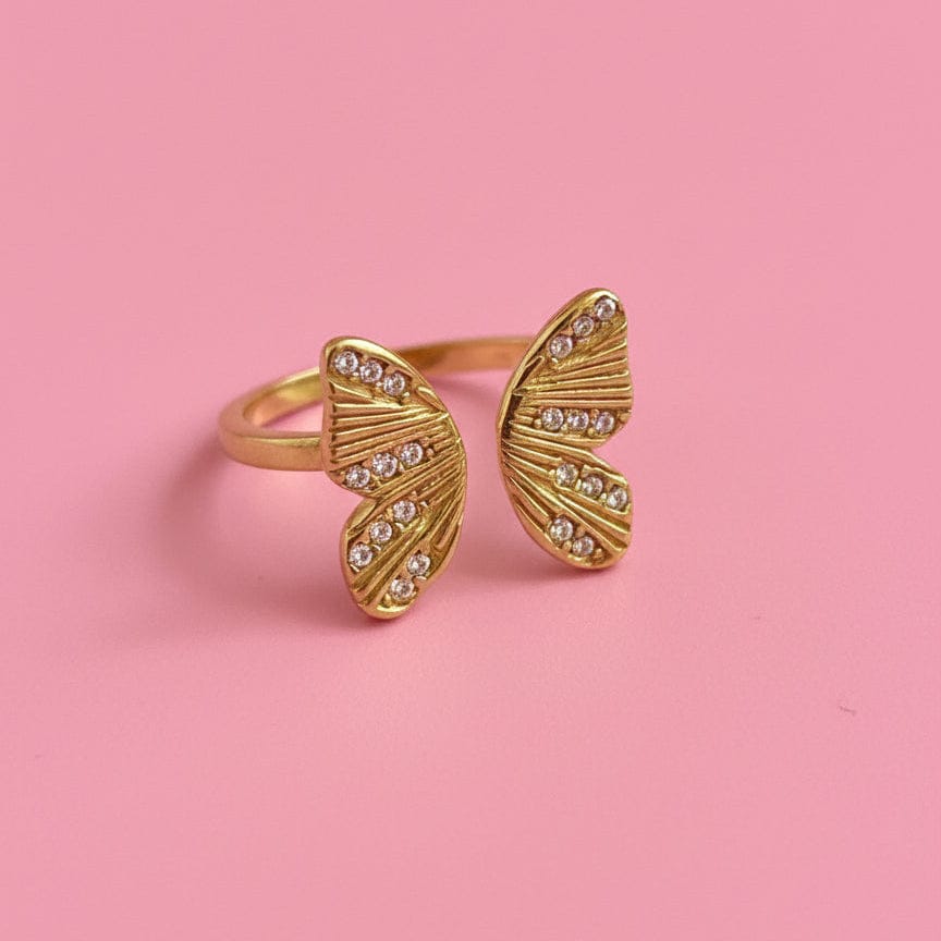 Gold butterfly-shaped ring with gemstones on a pink background