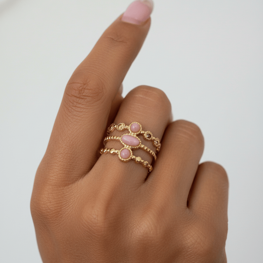 Hand wearing a gold ring with pink stones on a plain background