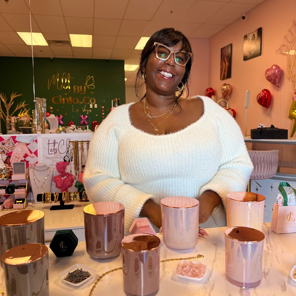 Woman in a white sweater sitting at a table with metallic containers and decorative items.